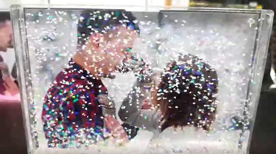 מסגרת אקריליק שקופה ומלבנית בצורת "כדור שלג", ובה תמונה של זוג מחובק המוקף בנצנצים ופתיתים כסופים המרחפים בנוזל